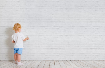 Baby boy with paint brush standing back near brick wall