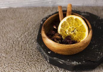Dry ingredients spices for mulled wine in wooden bowl on grey concrete background