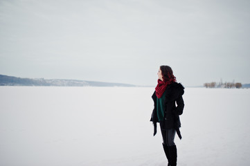 Fototapeta na wymiar Brunette girl in green sweater and red scarf outdoor frozen lake on evening winter day.
