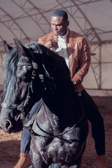 african american man riding black horse in hangar