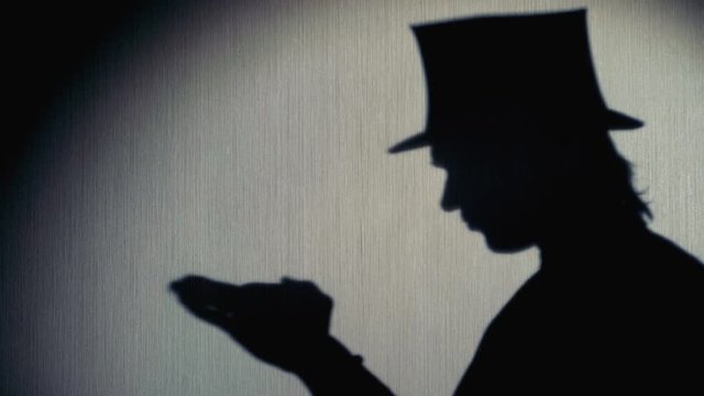 Silhouette of magician in a top hat showing a trick.
