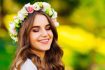 Naklejka premium Close-up of a beautiful girl with a wreath of flowers on her head that closed her eyes and smile