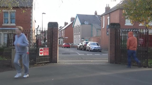 An old woman jogs into a park , Newcastle upon Tyne, UK