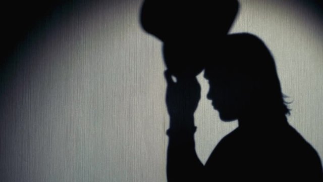 Magician silhouette in a top hat showing a trick. Close-up.
