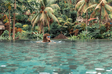Happy young woman in a tropical infinity pool. Luxury resort on Bali island.