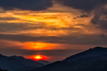 Naklejka na ściany i meble Beautiful landscape of a big setting sun over the silhouette of the mountains, Salciua, Romania