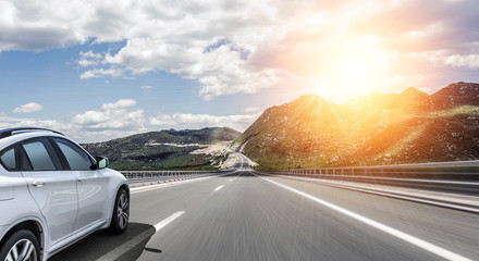 A white car rushing along a high-speed highway in the sun.