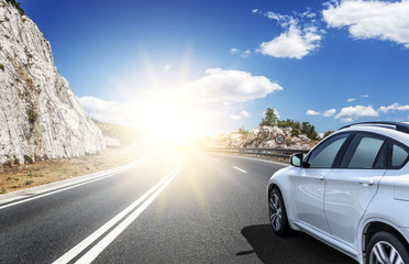 A white car rushing along a high-speed highway in the sun.