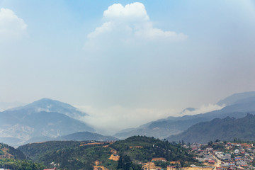 Fototapeta na wymiar Sa Pa landscape with city, mountains, fog and trees the view from above from Sam Bay Cloud Yard in summer at Ham Rong Mountain Park in Sa Pa, Vietnam.