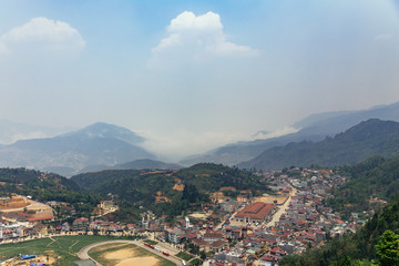 Fototapeta na wymiar Sa Pa landscape with city, mountains, fog and trees the view from above from Sam Bay Cloud Yard in summer at Ham Rong Mountain Park in Sa Pa, Vietnam.