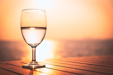 Silhouette glass of wine on a wooden table with  seascape and skyline in the evening with sunset tone style.