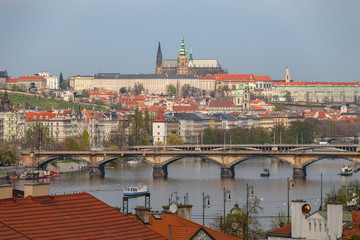 View of Vltava river in Prague and Charles bridge and the Castle over red roofs, Czech Republic