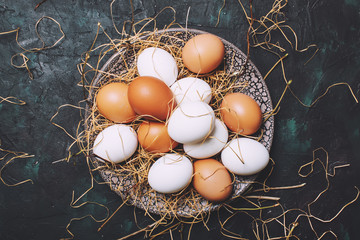 Multicolored chicken eggs with straw and branches, spring Easter composition, black background, top...