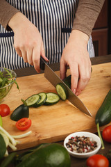 Woman cutting cucumber for fresh salad side view