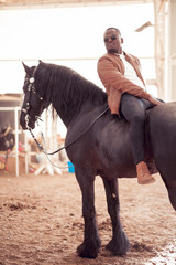african american man riding black horse in hangar
