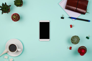 Business flatlay with smartphone with black copyspace screen, succulents and cactuses and other business accessories. Mint color background. Top view