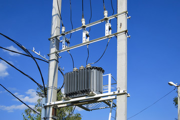 An electrical distribution transformer with cooling fins is located on the pole. Against the blue...