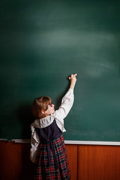 girl in school uniform painting with chalk on a blackboard