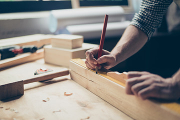 Cropped close up photo of foreman's hands holding a red pencil and measuring a wooden plank with a ruler on table, filing around on the table