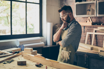 Pensive hardworking thoughtful serious concentrated minded cabinet-maker standing near table with...
