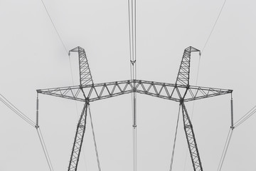 Hi-voltage electric power lines in a wintry foggy landscape, black and white photo.