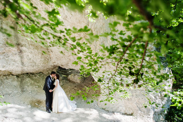 Wedding couple against cave at summer day.