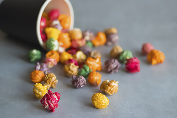 Multicolored popcorn and black paper cup on gray background.