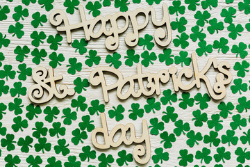 Happy St Patrick's Day wooden lettering with handmade paper shamrocks over a rustic wooden...