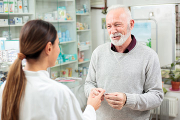 medicine, pharmaceutics, health care and people concept - happy senior man customer buying medications at drugstore