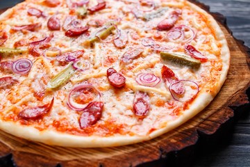 Yummy pizza with salami, onions and gherkins served on chopped wood. Food background, restaurant or pizzeria concept