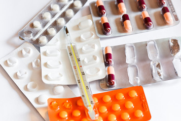 Termometer and medical pills on white background