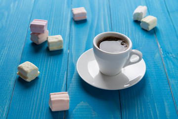 a cup of black coffee on blue boards surrounded by scattered marshmallows