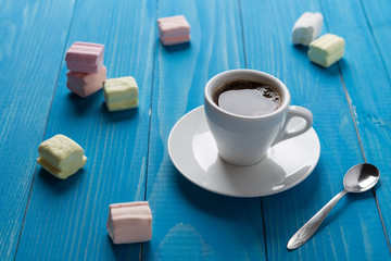 a cup of black coffee on blue boards surrounded by scattered marshmallows