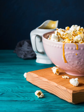 Popcorn with salted caramel in pink bowl on wooden board on dark background