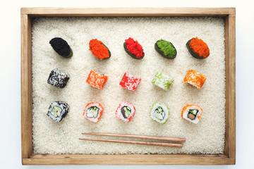Sushi rolls and gunkan in wooden frame on rice
