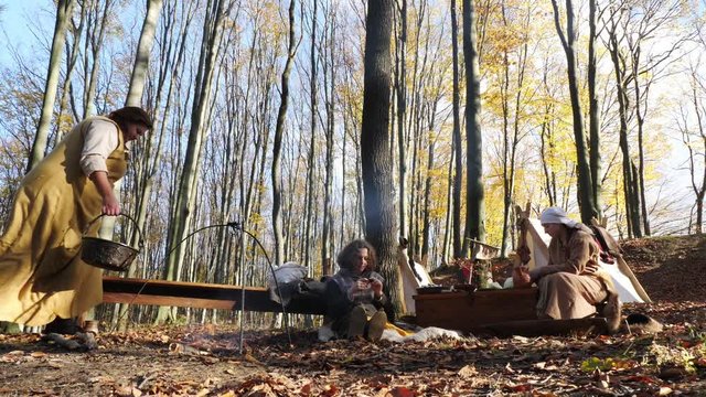 A woman hangs a cauldron on an open fire in a Viking camp.