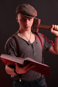 A young stylish guy with a big hammer reading big boock