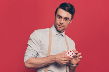 Professional, cunning magician, poker player, gambler in casual outfit, glasses with serious expression, holding deck of cards, standing over red background