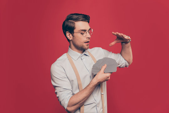 Professional, cunning magician, illusionist, gambler in casual outfit, glasses, holding set deck of cards, making performance, show trick standing over red background