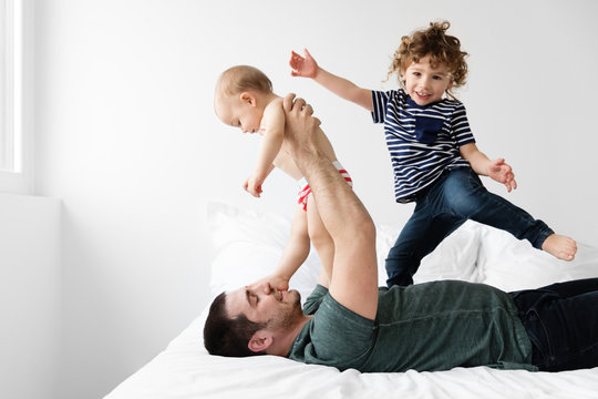 Dad Wrestling On Bed With Son And Baby