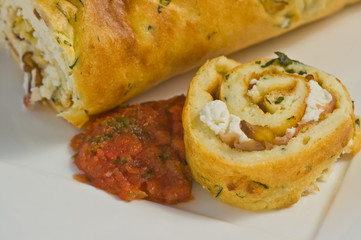 Close up of freshly baked, slice of rolled basil souffle with red pepper coulis on a rectangular white plate