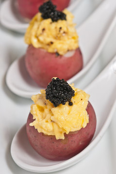 Close up, front view, freshly prepared red potato filled with scrambled eggs and toped with caviar on porcline spoons