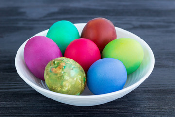 White plate of Easter multicolored boiled eggs on black wood