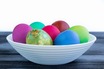 White plate with Easter multicolored boiled eggs on black wood
