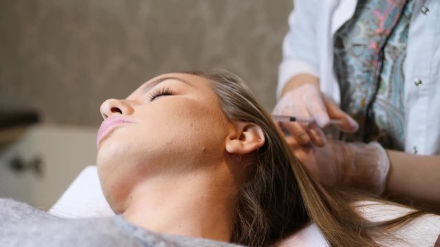 Woman in cosmetology cabinet. Cosmetologist is doing injection. woman receives an injection in the head. The concept of mesotherapy.