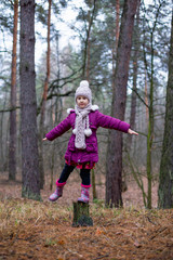 Little girl posing near the old stump in autumn forest.