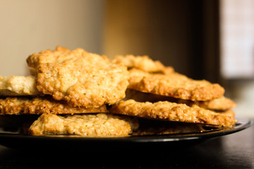 Tasty glossy brown homemade oatmeal cookies on black plate, side view. Delicious peanut oatcakes, healthy sweet home-baked products