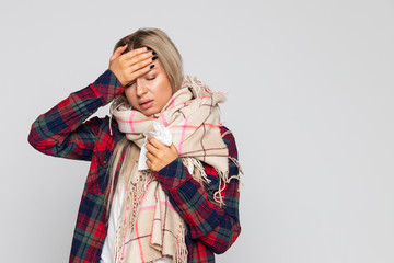 Woman in checked shirt, wrapped scarf having headache and holding glass with water, touching her forehead and closed eyes. Cold season, flu concept