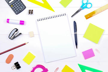 A blank notebook page surrounded by stationery on a white wooden table. Copy the space.