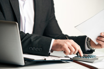 Businessman's hands using calculator and Financial data analyzing on white desk at the office, close-up